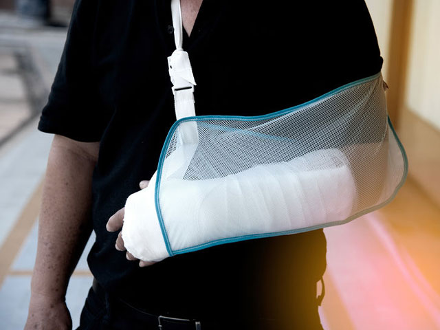 A person wearing a black shirt has their bandaged arm supported in a white mesh sling.