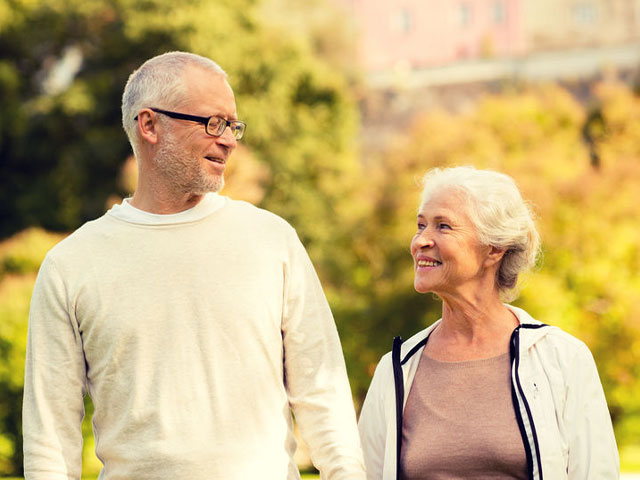 An older woman and a middle-aged man walk outdoors together, smiling at each other on a sunny day.